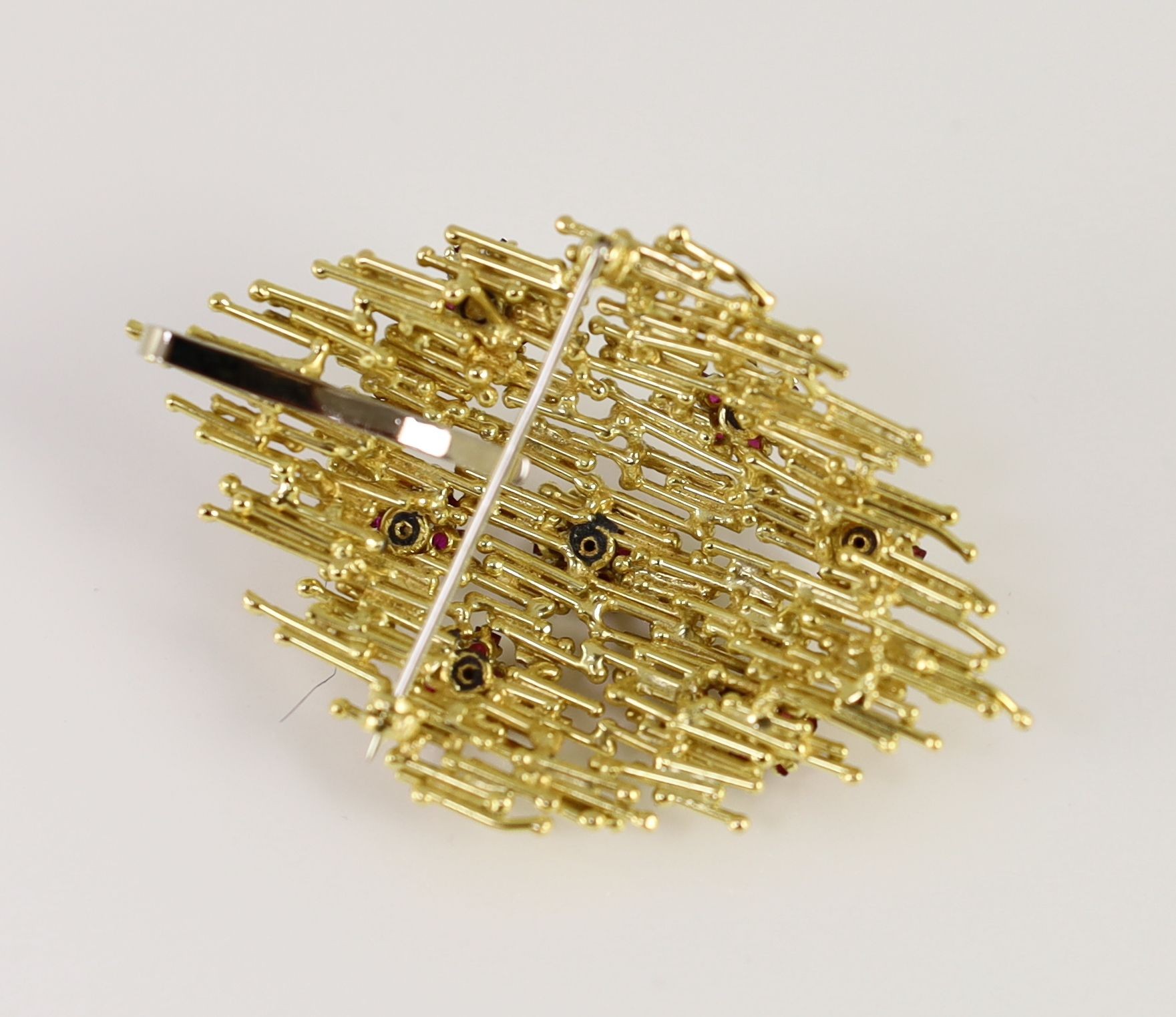 A 1970's textured gold, ruby and diamond cluster set modernist pendant brooch, in the manner of Andrew Grima